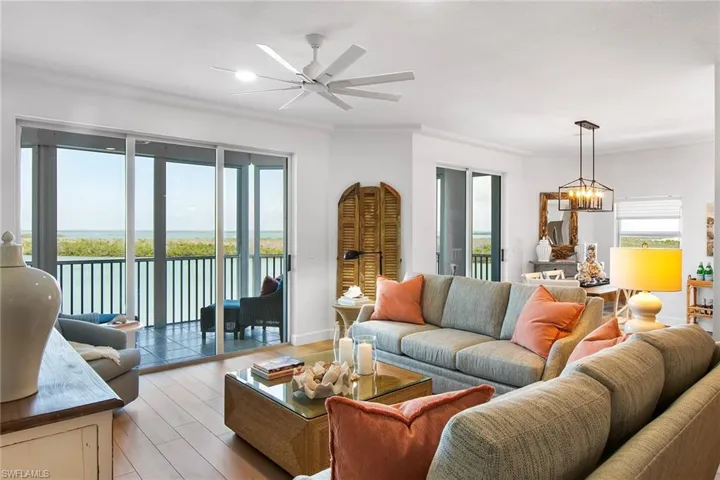 Living area featuring ceiling fan with notable chandelier, baseboards, crown molding, and light wood-style floors