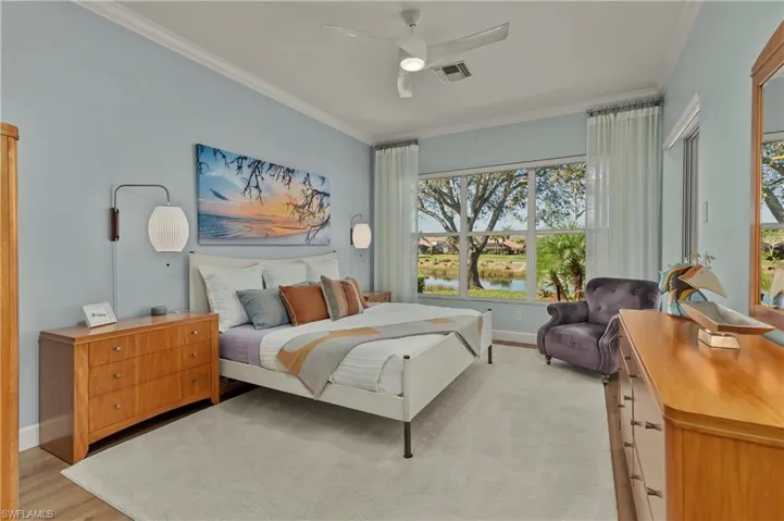 Bedroom with light wood-type flooring, ornamental molding, ceiling fan, and a water view