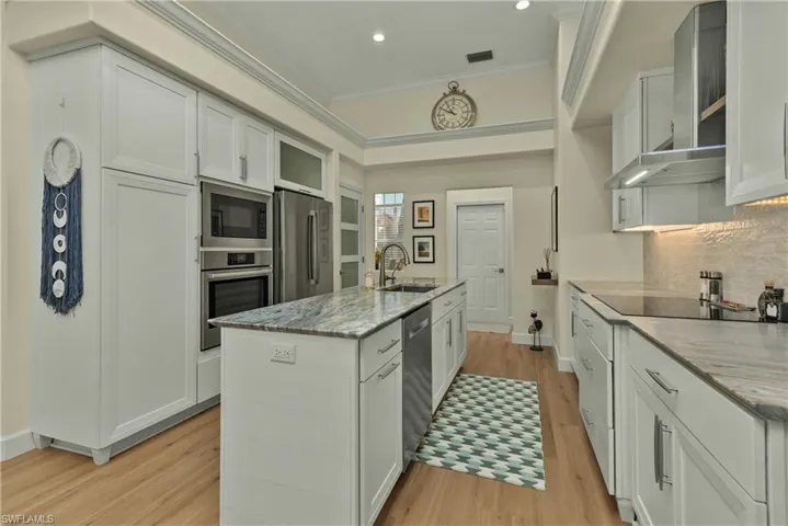 Kitchen featuring sink, a center island with sink, appliances with stainless steel finishes, light stone countertops, and white cabinets