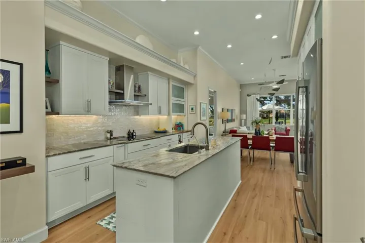 Kitchen featuring sink, a kitchen island with sink, light stone counters, white cabinets, and wall chimney exhaust hood