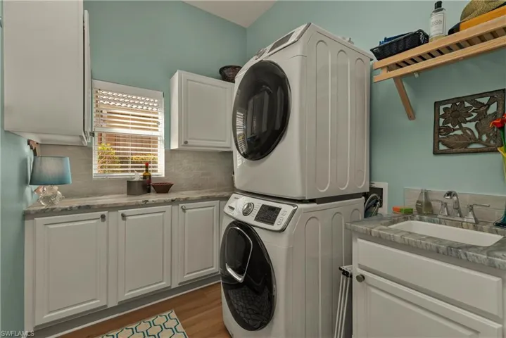 Laundry area with stacked washer / dryer, sink, cabinets, and dark hardwood / wood-style floors