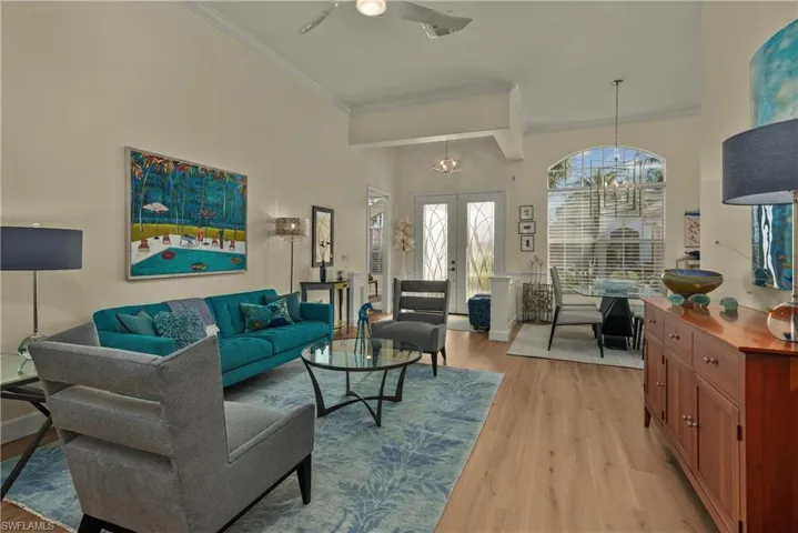 Living room with french doors, light hardwood / wood-style flooring, ornamental molding, a towering ceiling, and ceiling fan with notable chandelier