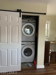 Laundry area with a barn door, new stacked washing machine and dryer, and dark wood-style flooring