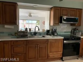 Kitchen with newer cabinetry, electric range oven, light quartz countertops, stainless steel microwave, and a ceiling fan
