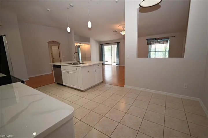 Kitchen featuring white cabinetry, an island with sink, light tile patterned floors, hanging light fixtures, and ceiling fan