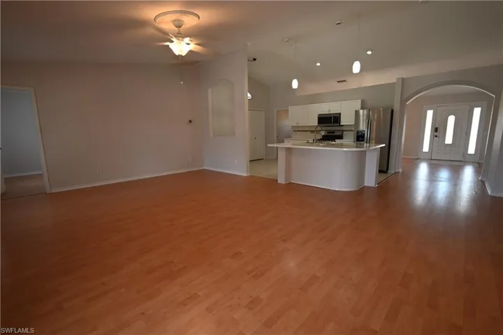 Kitchen featuring open floor plan, white cabinets, vaulted ceiling, arched walkways, and a ceiling fan