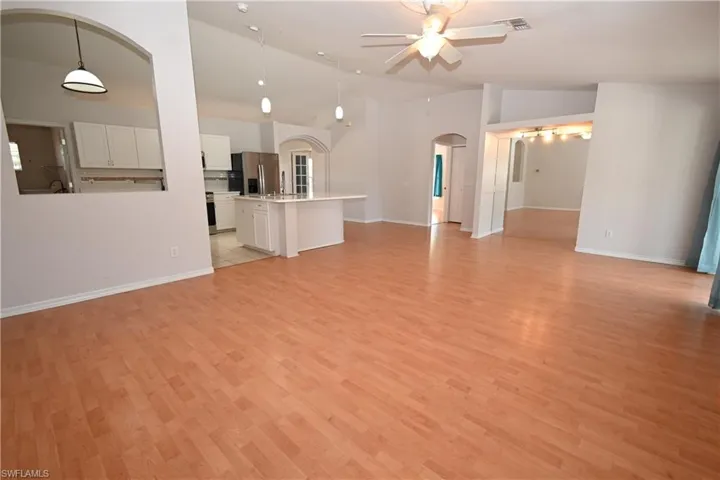 Unfurnished living room featuring arched walkways, a ceiling fan, vaulted ceiling, and light wood finished floors