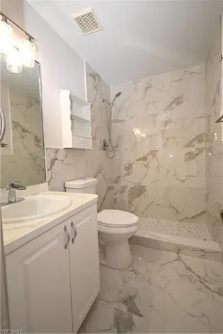 Bathroom featuring tile walls, vanity, a marble finish shower, and light marble finish flooring