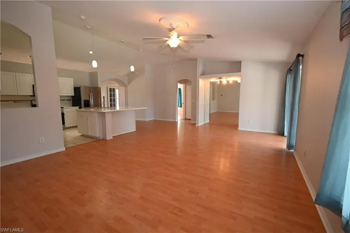 Unfurnished living room featuring a ceiling fan, vaulted ceiling, arched walkways, and light wood-style flooring