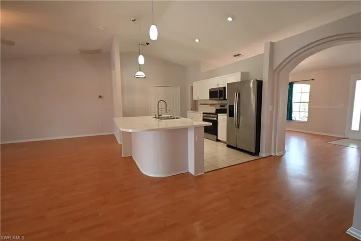 Kitchen featuring arched walkways, white cabinets, stainless steel appliances, light countertops, and a kitchen island with sink