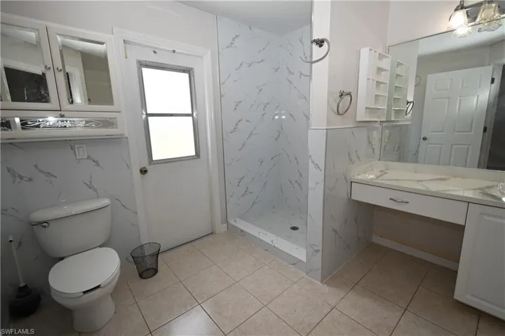 Bathroom with a marble finish shower, vanity, and light tile patterned floors