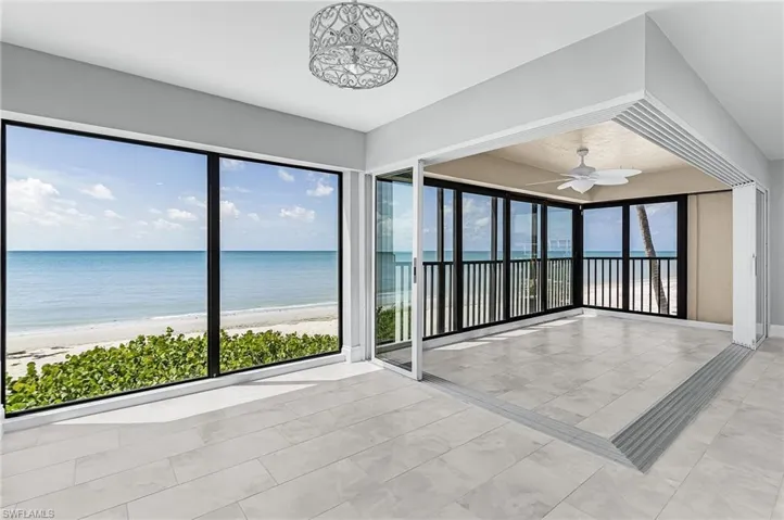 Empty room featuring view of water and beach, ceiling fan, and light tile patterned floors