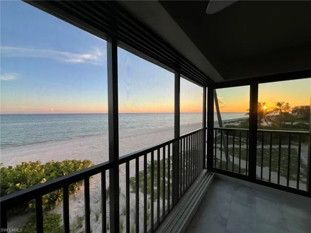 Balcony at dusk with view of water and beach and ceiling fan