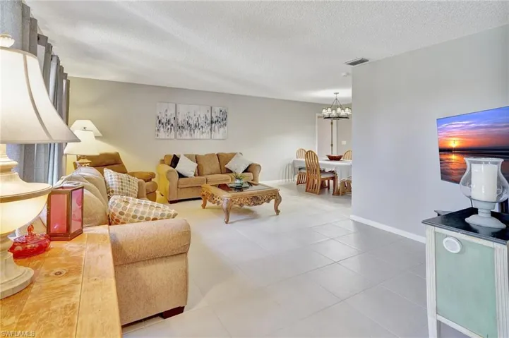 Living area with a textured ceiling, a chandelier, visible vents, baseboards, and tile patterned floors
