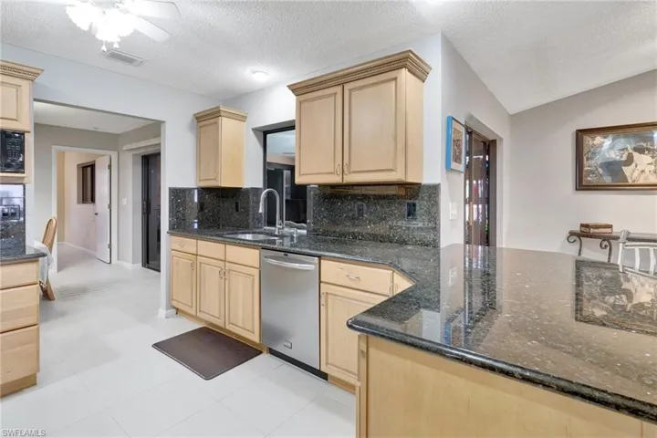 Kitchen featuring light brown cabinetry, backsplash, dishwasher, and a sink