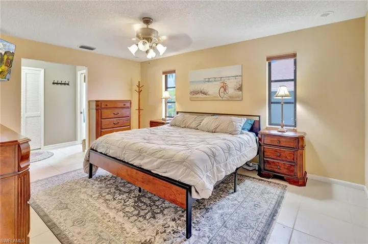 Bedroom featuring a textured ceiling, light tile patterned floors, visible vents, baseboards, and a ceiling fan