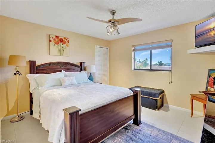 Tiled bedroom with a textured ceiling, a closet, a ceiling fan, and baseboards