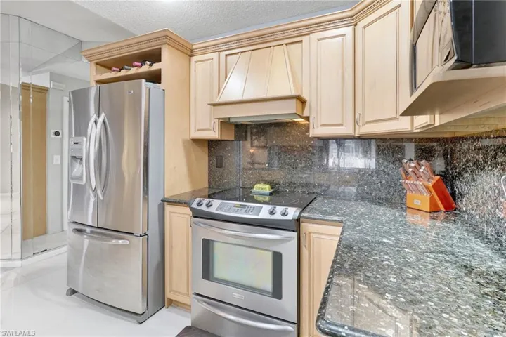 Kitchen with light brown cabinets, backsplash, appliances with stainless steel finishes, and premium range hood