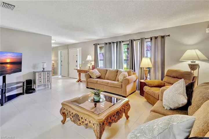 Living room with a textured ceiling, visible vents, and light tile patterned floors