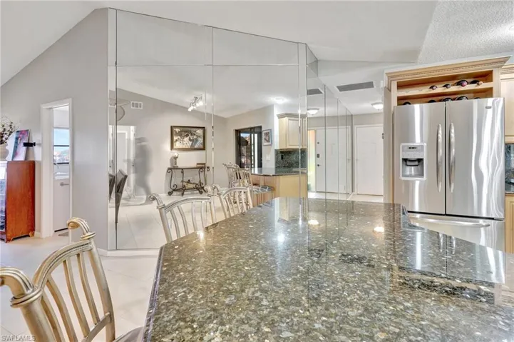 Kitchen with light tile patterned floors, dark stone counters, lofted ceiling, and stainless steel fridge with ice dispenser
