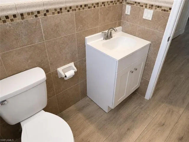 Bathroom featuring a white toilet, floor-to-ceiling tiled walls with decorative mosaic accent, and a white vanity with an integrated sink and brushed nickel faucet