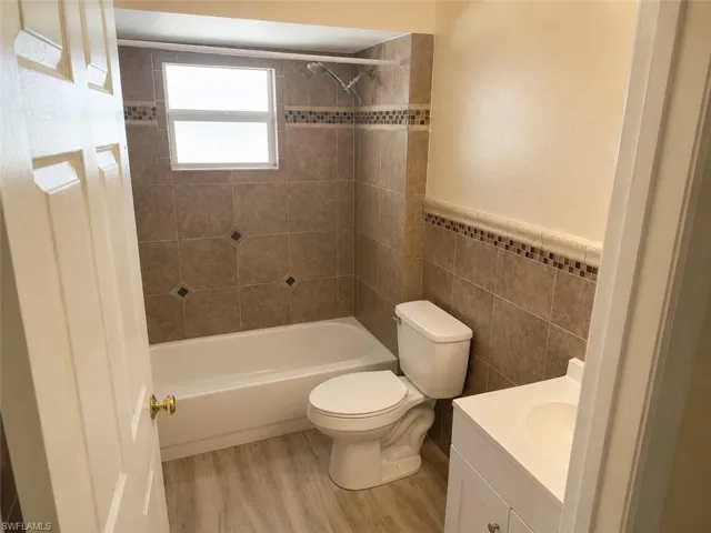 Full bathroom featuring an integrated bathtub and shower with brown tile surround, a white vanity with integrated sink, and wood-finish flooring
