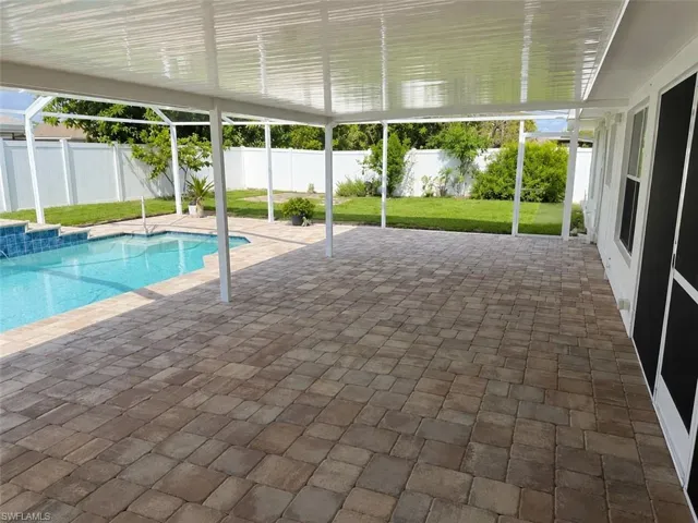 Covered patio featuring multi-toned paver flooring, a refreshing swimming pool with tiled steps, and a white privacy fence encompassing the backyard