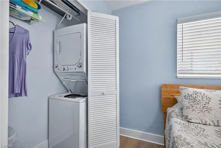 Integrated stacked washer and dryer unit, louvered closet doors, window with horizontal blinds, wood-finish flooring