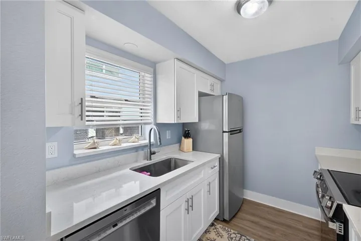 Kitchen featuring white cabinetry, stone countertops, stainless steel appliances, a stainless steel sink, and wood-finish flooring