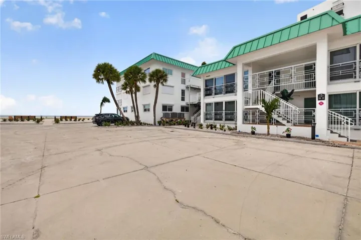 White exterior with a green roof, multiple balconies, exterior staircases, and mature palm trees