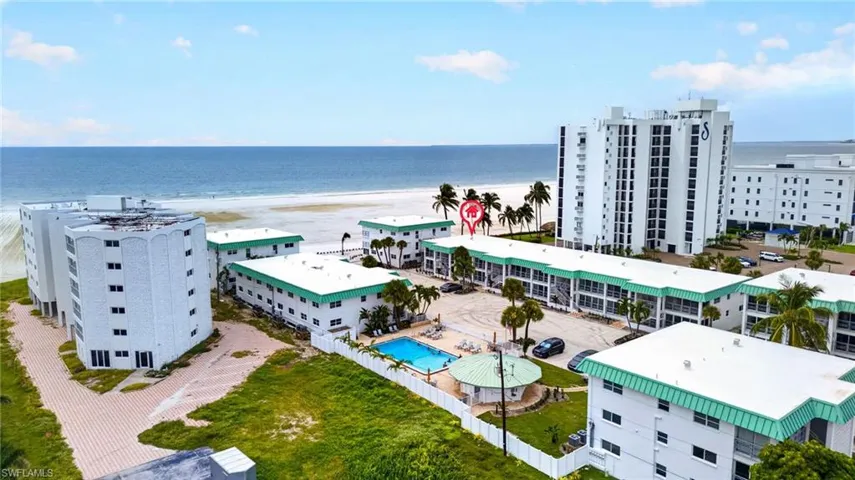 Beachfront resort-style community featuring multiple contemporary residential towers with turquoise-accented architectural elements, resort-amenity pool deck, manicured landscaping with mature palm trees, direct oceanfront access, and expansive sandy beach frontage