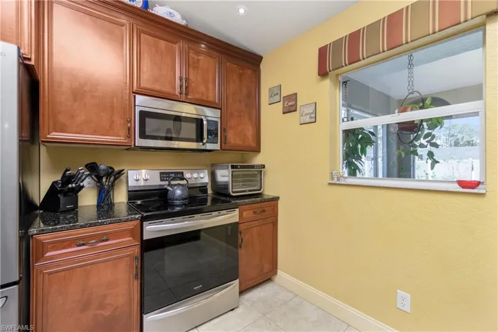 Kitchen with light tile patterned floors, a toaster, baseboards, appliances with stainless steel finishes, and dark stone countertops