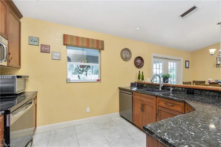 Kitchen with visible vents, dishwasher, brown cabinets, dark stone countertops, and a sink