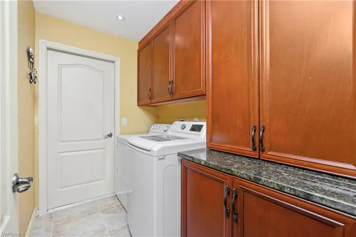 Clothes washing area featuring cabinet space, washing machine and dryer, and light tile patterned floors