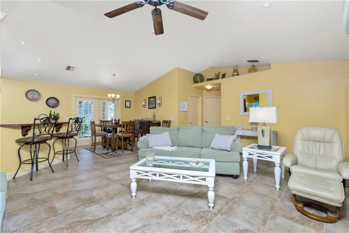 Living room with lofted ceiling, visible vents, and ceiling fan with notable chandelier