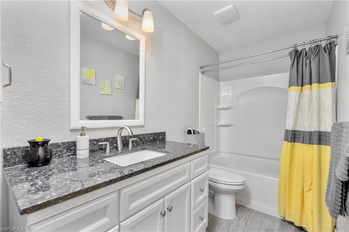 Full bath featuring toilet, a textured wall, shower / tub combo, and vanity