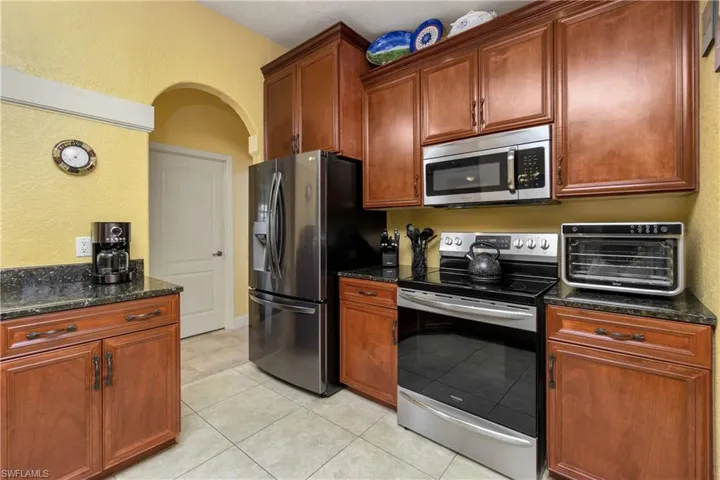 Kitchen featuring stainless steel appliances, dark stone counters, a toaster, and light tile patterned floors