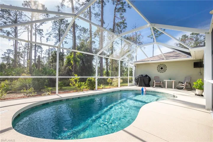 Outdoor pool with a patio area, glass enclosure, and grilling area
