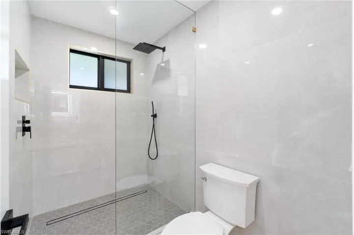Primary bathroom featuring floor to ceiling tile walls, toilet, and a walk in shower
