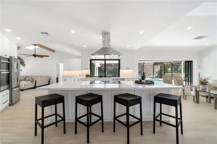 Kitchen with a large island, a kitchen bar, island exhaust hood, and white cabinetry
