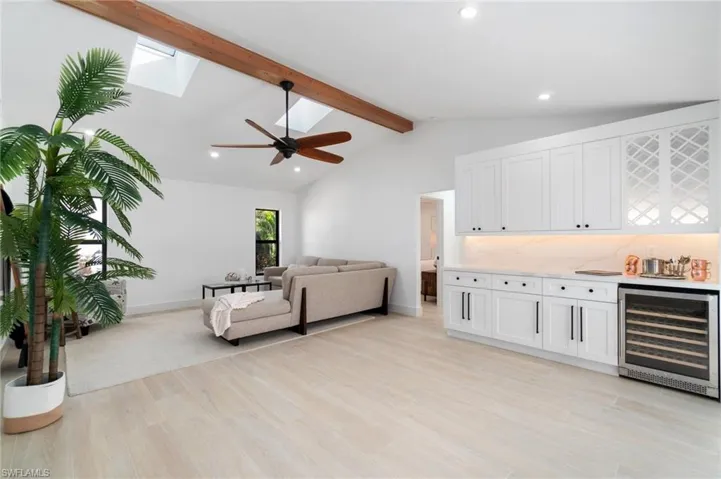 Living area with lofted ceiling with beams, light wood-style flooring, wine cooler, and a bar