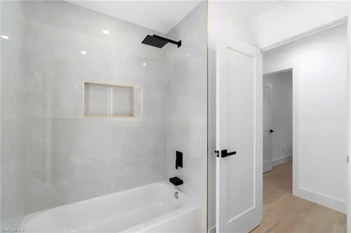 Guest bathroom featuring bathtub / shower combination, tile to ceiling, and wood finished floors