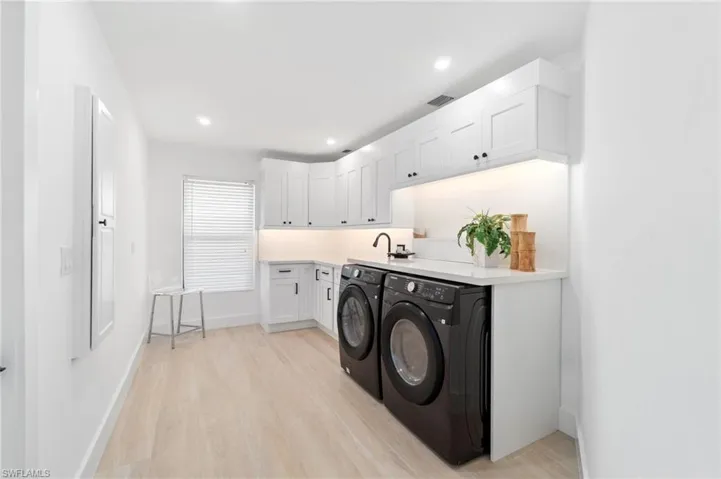 Laundry room featuring recessed lighting, white slow-close cabinets, quartz countertops and matching quartz backsplash, light wood-style floors, and washing machine and dryer
