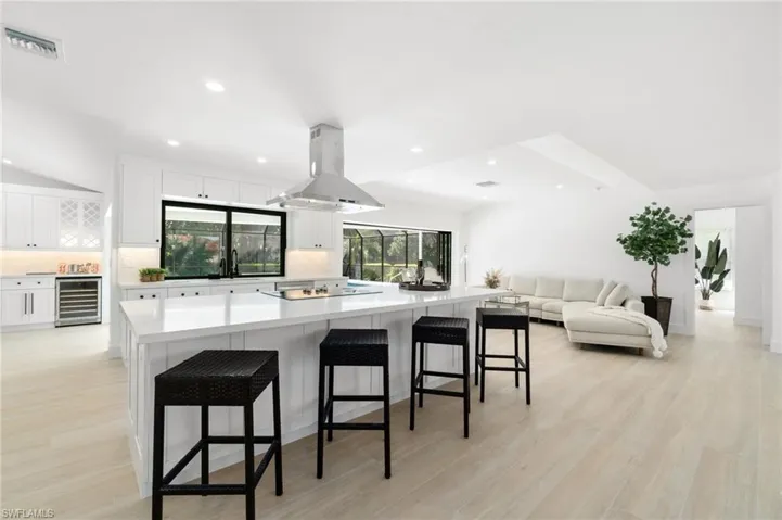Kitchen featuring wine cooler, white cabinetry, island exhaust hood, and a kitchen breakfast bar