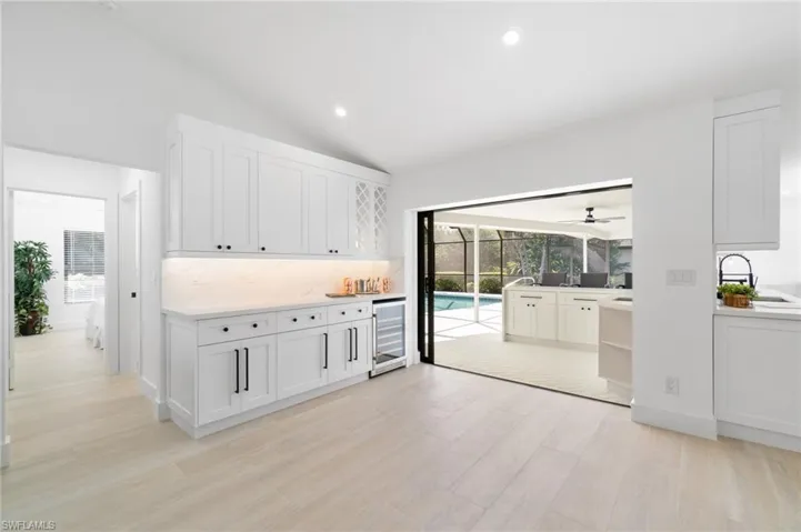 Bar area featuring light wood finished floors, beverage cooler, white slow-close cabinets, and quartz countertops with matching quartz backsplash