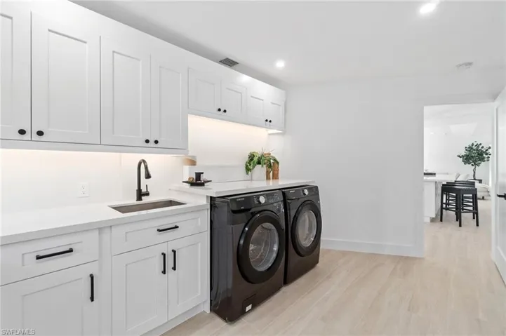 Laundry room with recessed lighting, a sink, light wood-style floors, quartz countertops and matching backsplash, white cabinetry and washing machine and clothes dryer