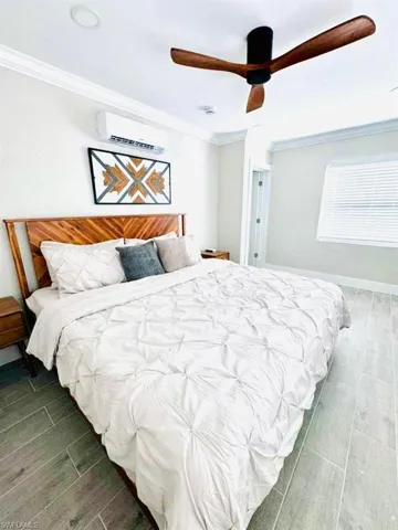 Bedroom featuring wood tiled floors, ornamental molding, a ceiling fan, and an AC wall unit