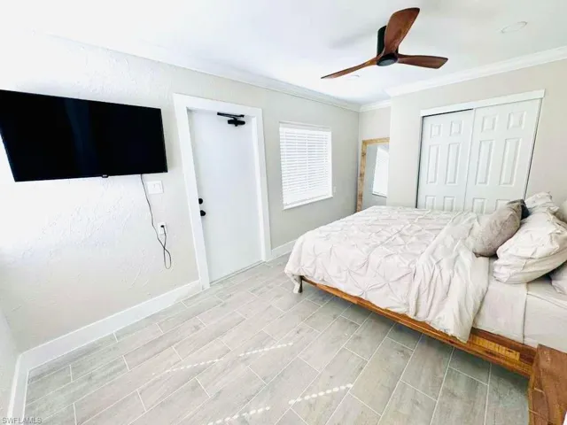 Bedroom with ornamental molding, a closet, a ceiling fan, and wood tiled floors