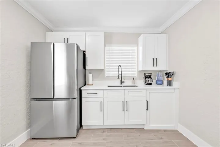 Kitchen with a textured wall, freestanding refrigerator, ornamental molding, white cabinetry, and wood tiled floors
