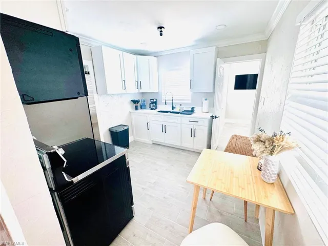 Kitchen with white cabinetry, black electric range oven, light countertops, crown molding, and light wood-type flooring